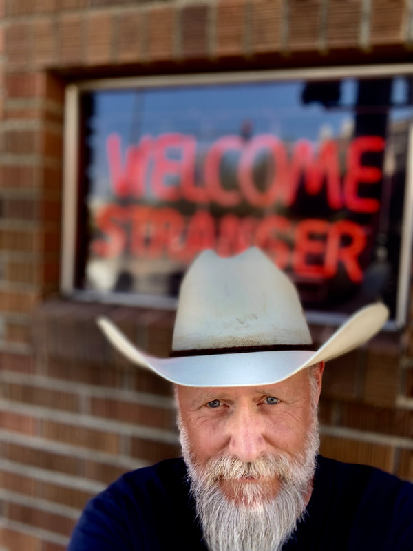 J Shogren stands in front of a neon WELCOME STRANGER sign